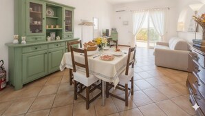 A dining area with a table set for four, a green cabinet with glass doors, and a sofa in the background.