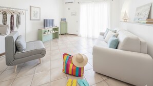 A living room with a grey sofa, a white sofa, a colorful bag, and a hat on the floor.