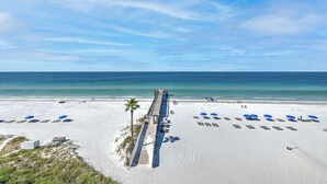A beach with a wooden pier extending into the ocean, rows of beach umbrellas, and a sandy beach area.