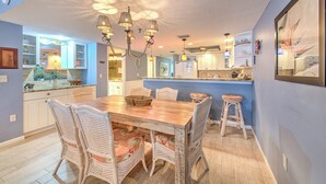 A spacious kitchen with white cabinetry, a wooden dining table, wicker chairs, and a central island with a sink.