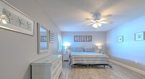 Un dormitorio con cama, mesitas de noche, ventilador de techo y decoración en la pared.