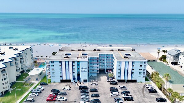 A hotel with a pool, parking lot, and beach view.