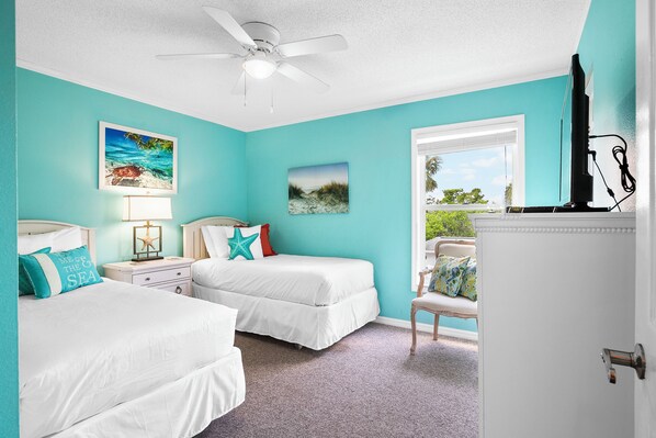 A bedroom with two beds, a ceiling fan, a window with a view, and artwork on the walls.