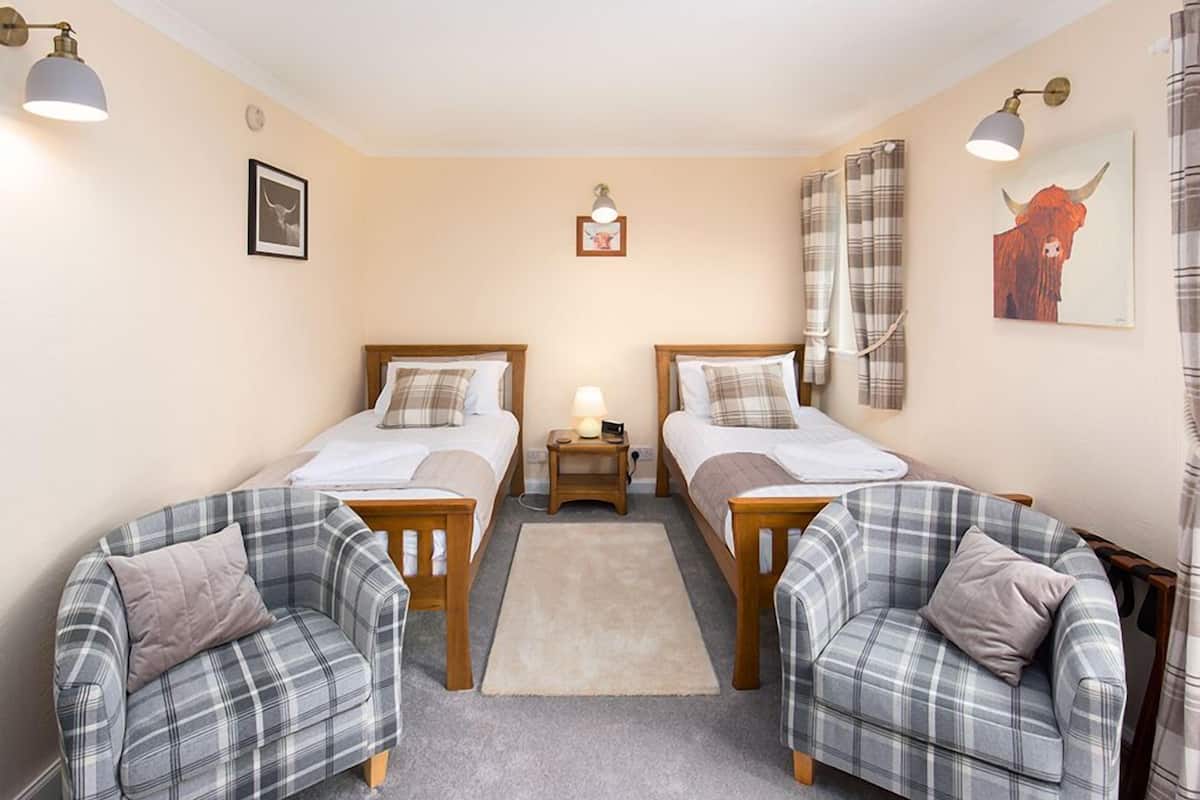 Une chambre avec deux lits, une petite table, une lampe et deux fauteuils à motifs écossais.
