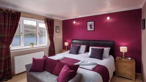 A bedroom with a bed, a nightstand, a lamp, a window with curtains, and a view of the outdoors. - Blythedale House (Fort William)