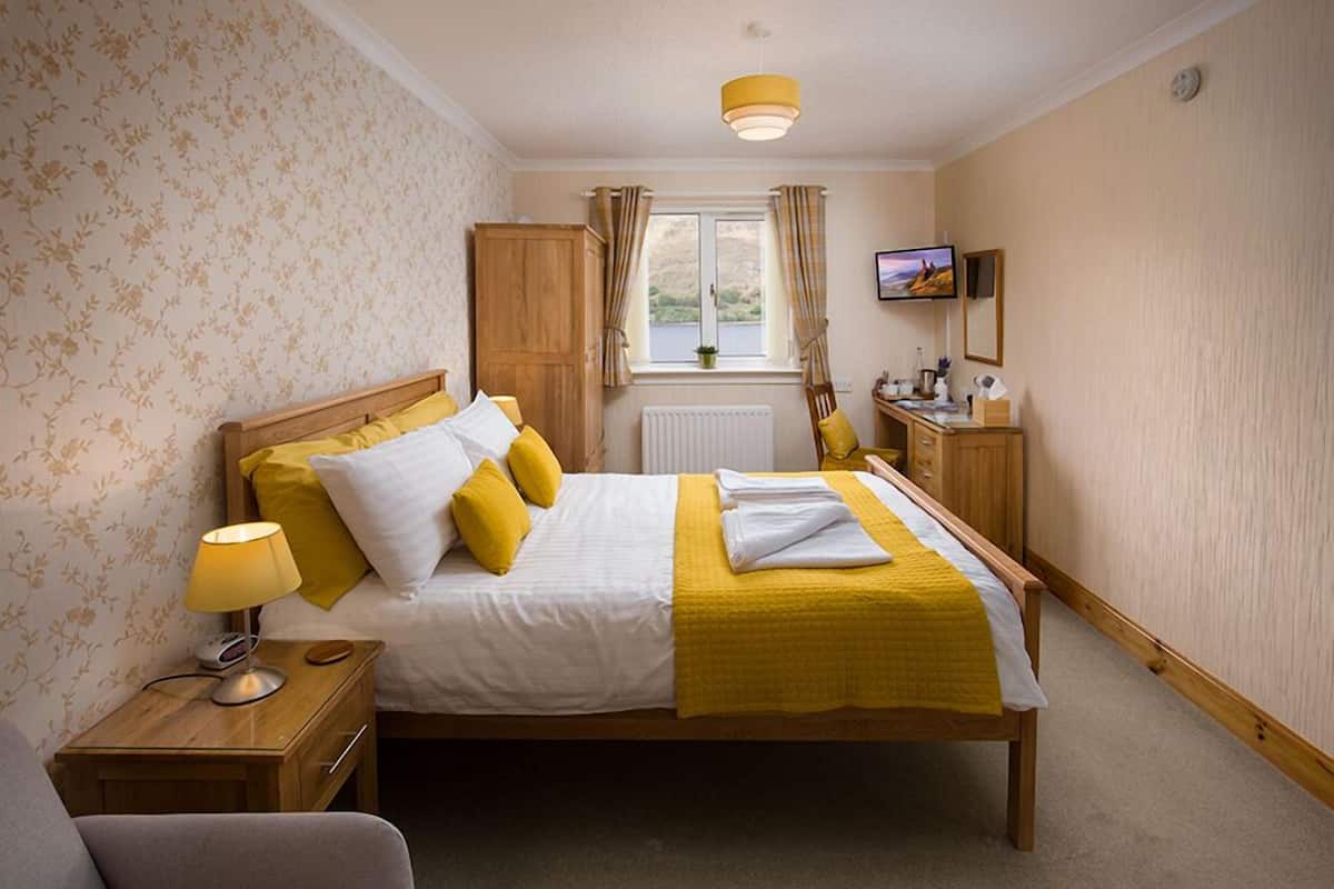 Une chambre à coucher bien rangée, avec un lit, une table de chevet, une lampe et un téléviseur posé sur un meuble.