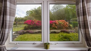 A window with two views of a garden, curtains, and a small potted plant on the windowsill. - Blythedale House (Fort William)