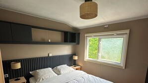 Un dormitorio con cama, mesitas de noche, ventana y lámpara en el techo.