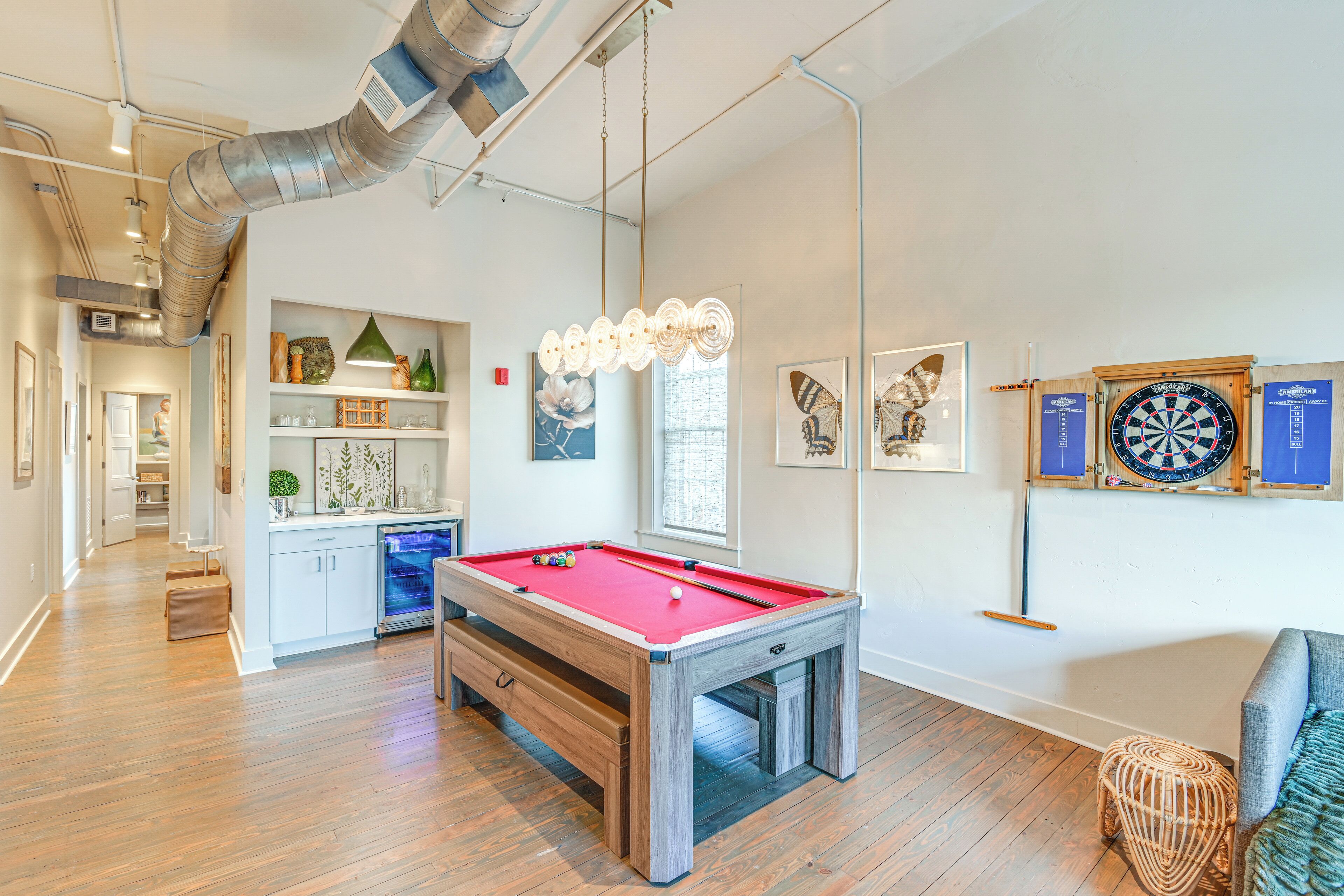 A pool table in a room with wooden flooring, a dartboard, and artwork on the walls.