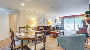 A dining area with a wooden table and chairs, a sofa, and a green armchair. There is a balcony with a view of trees. - Resort Condo w/ Marina Access in Williamsburg! (Williamsburg)