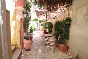 A narrow alleyway with a stone floor, a table with chairs, and potted plants. - Alley Studio 2 by Frangki (Aegina)