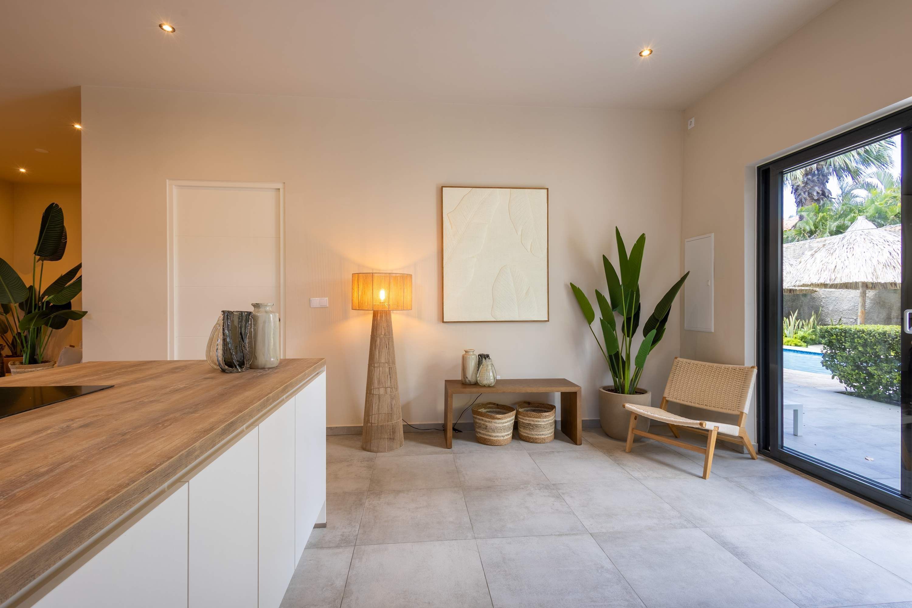 Una cocina moderna con encimera de madera, una lámpara de pie, un banco con cestas y una silla de mimbre.