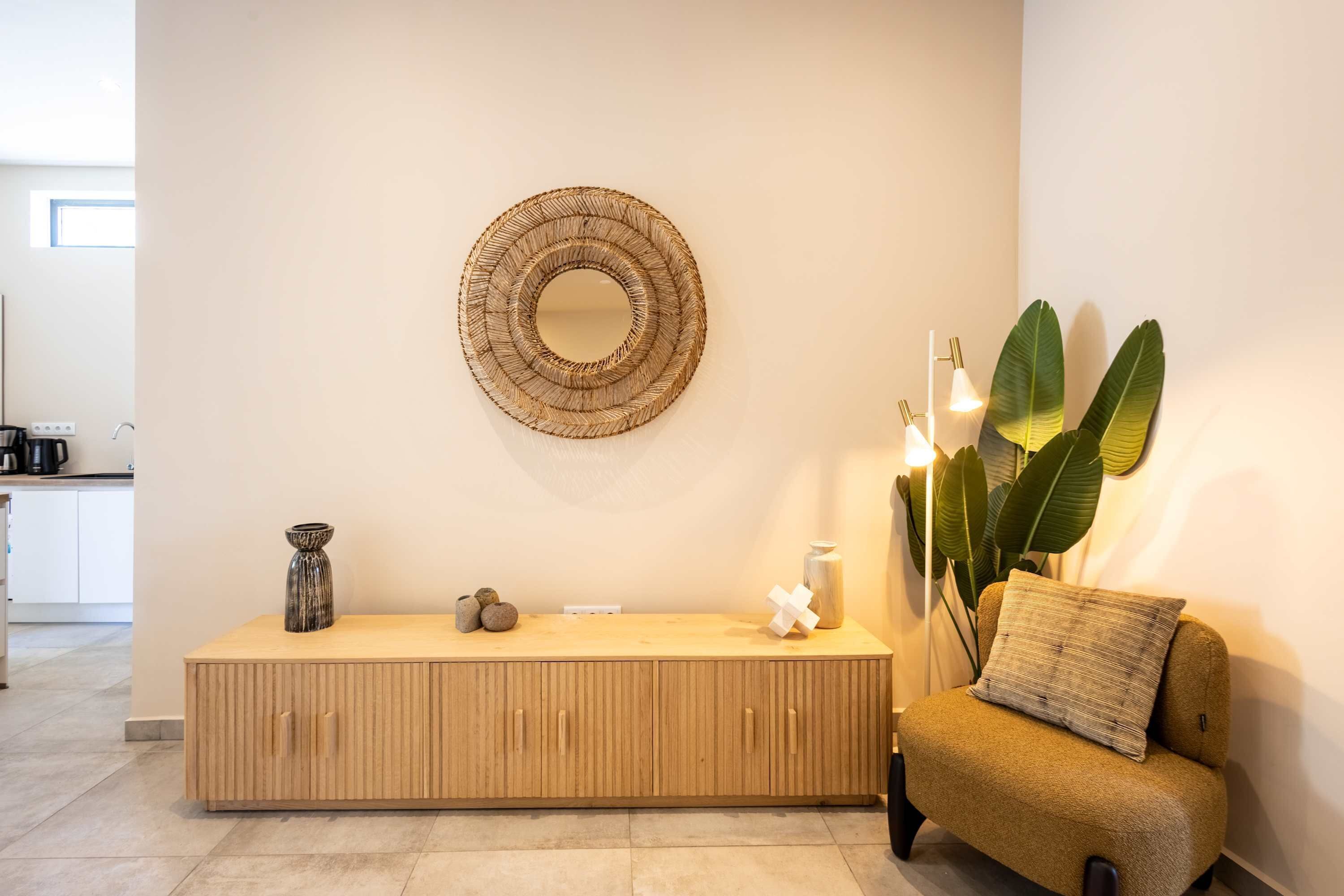 A modern living room with a wooden console table, a round woven mirror, a sofa, and a large plant.