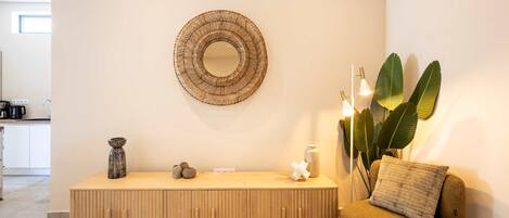 A modern living room with a wooden console table, a round woven mirror, a sofa, and a large plant.