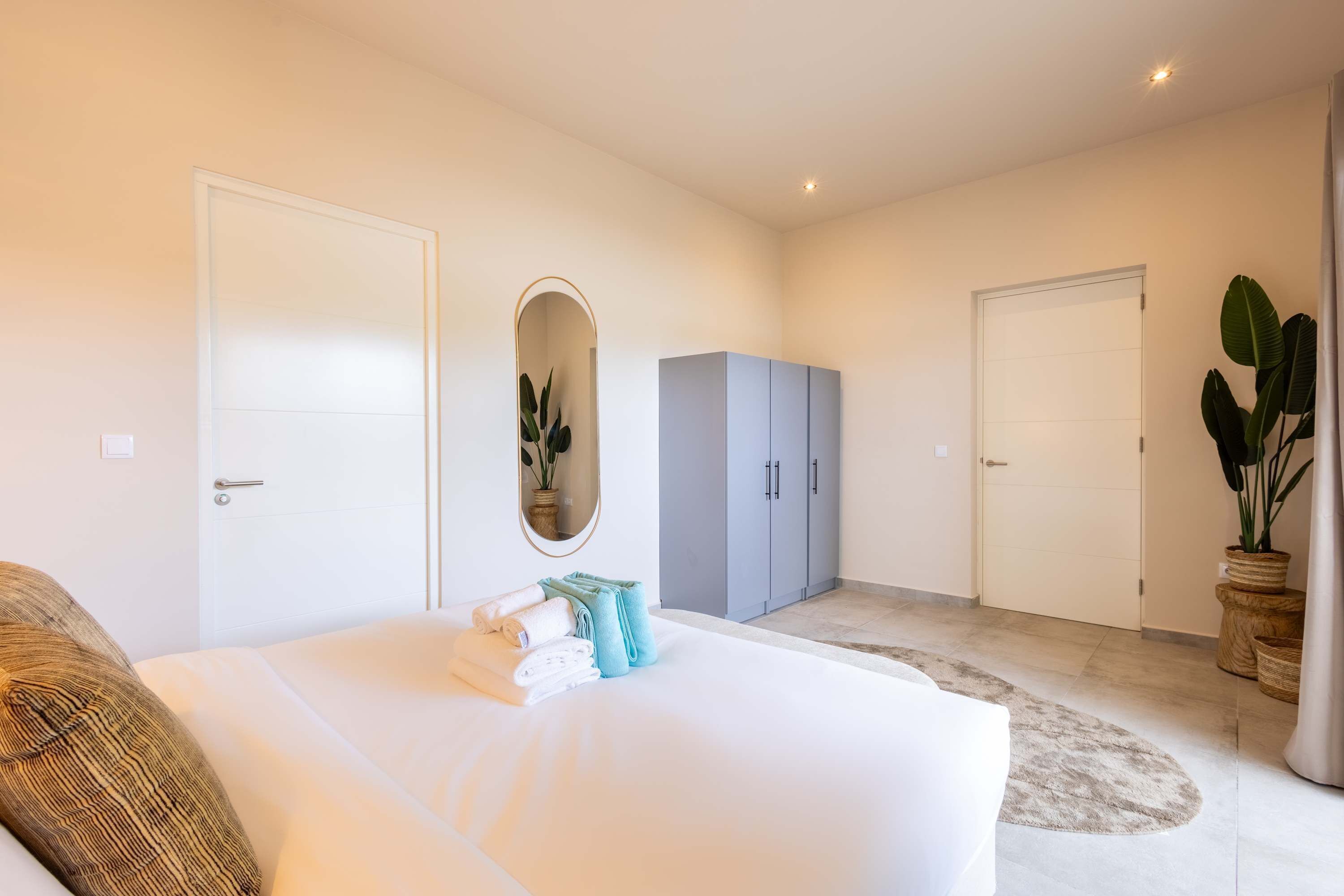 A bedroom with a large bed, a wardrobe, a mirror, and a potted plant.