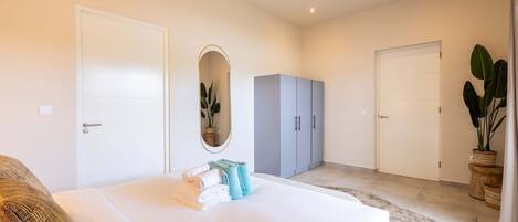 A bedroom with a large bed, a wardrobe, a mirror, and a potted plant.