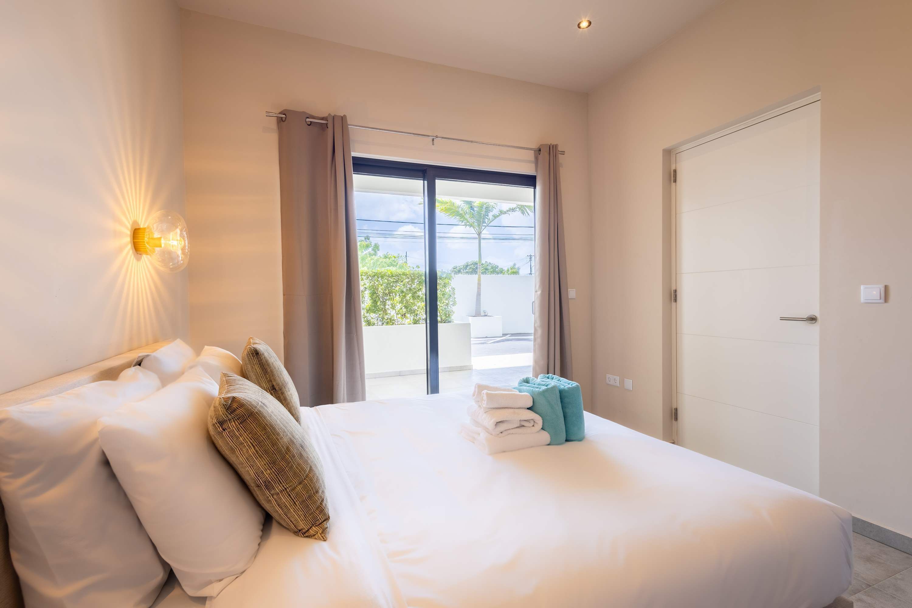 A hotel room with a bed, curtains, a view through the window, and a door.