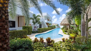 Een modern resort met een zwembad, weelderige begroeiing en een constructie met rieten dak.