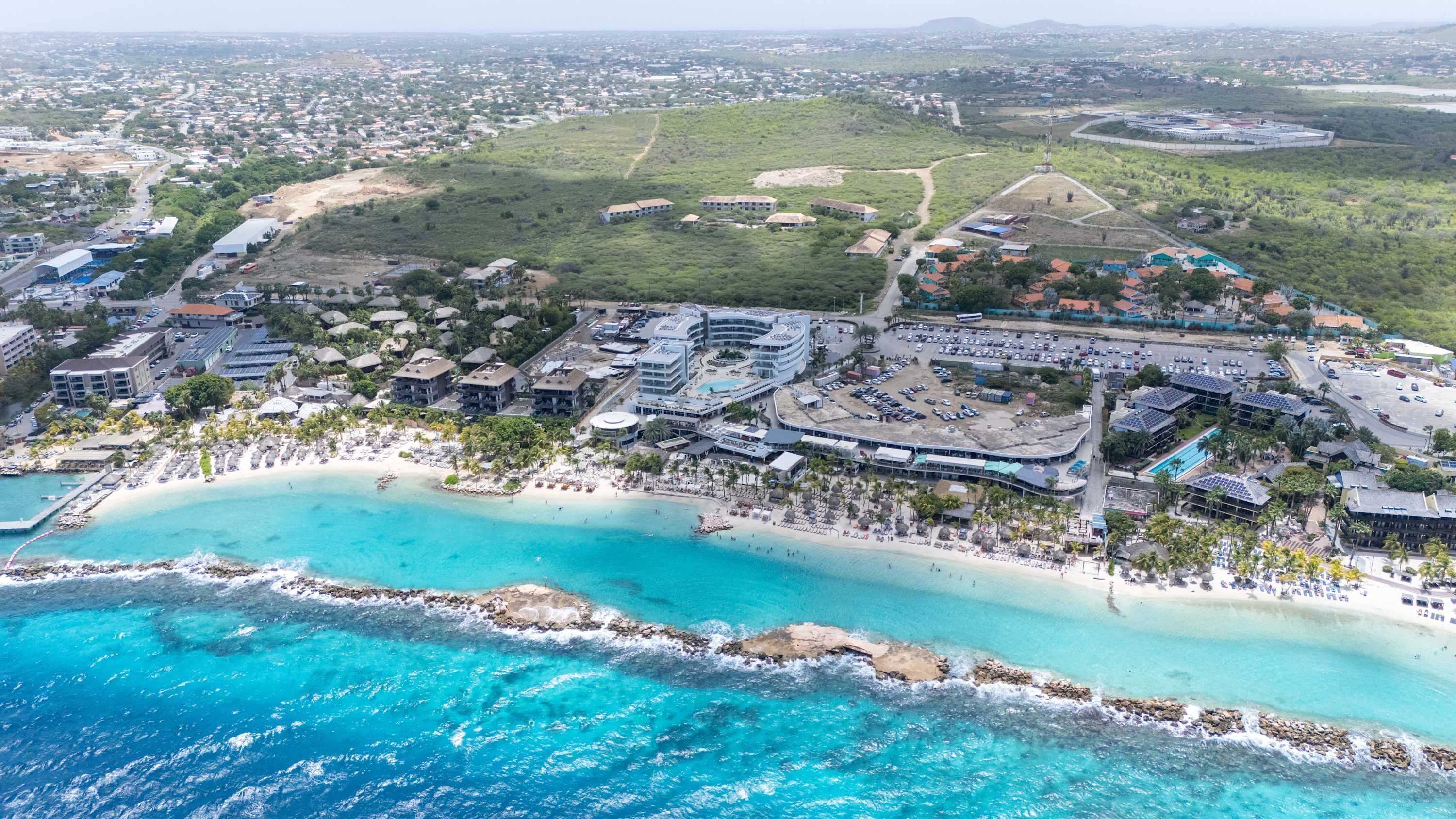 An aerial view of a coastal resort with a beachfront, multiple hotel buildings, and a parking area.