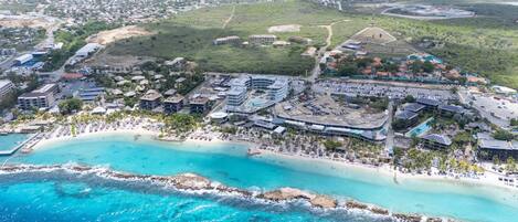 An aerial view of a coastal resort with a beachfront, multiple hotel buildings, and a parking area.
