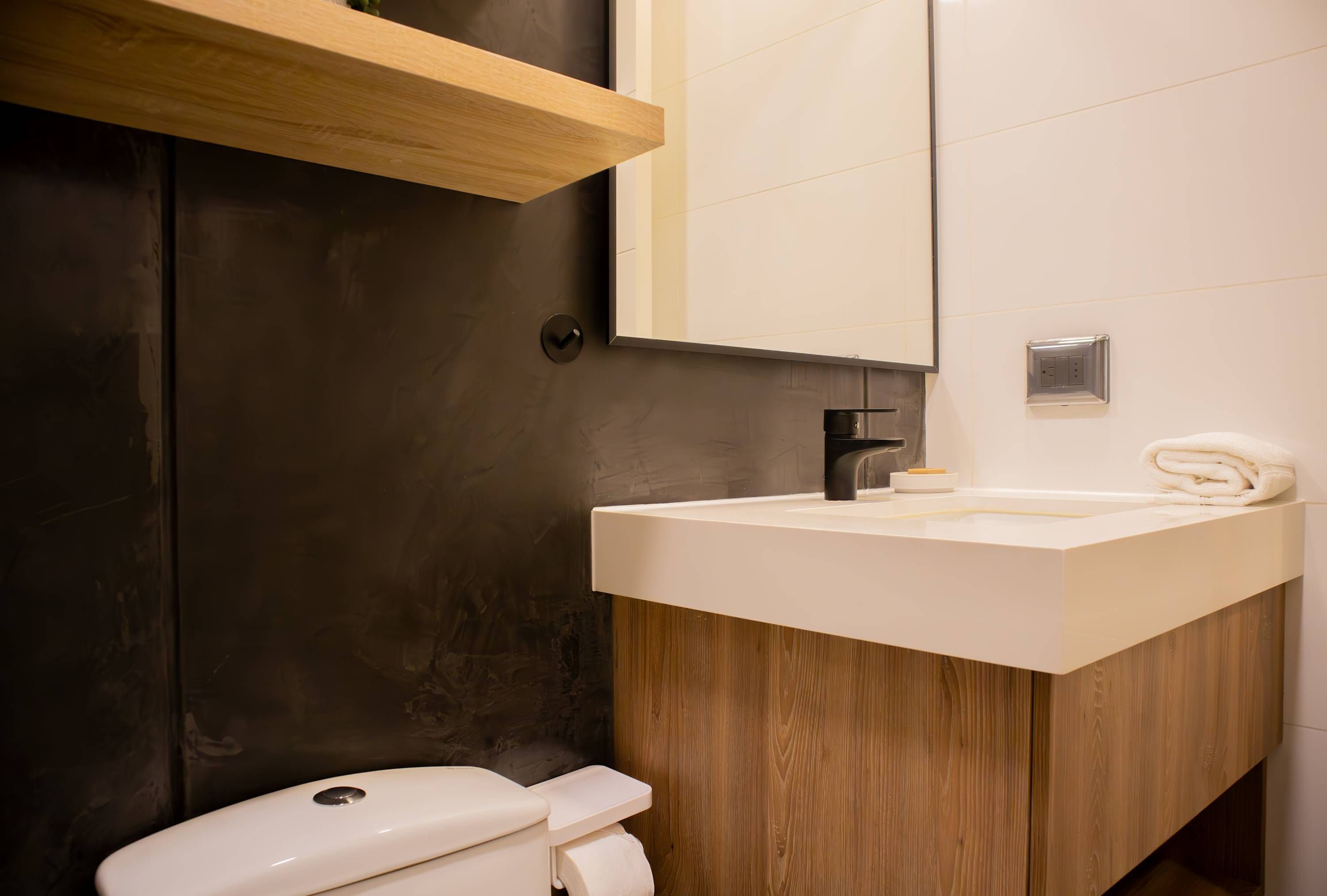 A modern bathroom with a wooden vanity, a white sink, and a toilet.