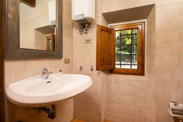 A bathroom with a white sink, a mirror, a window with a wooden frame, and a towel dispenser.