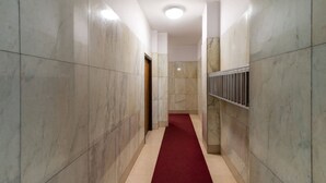 Un pasillo con paredes de mármol, alfombra roja y barandilla de metal.