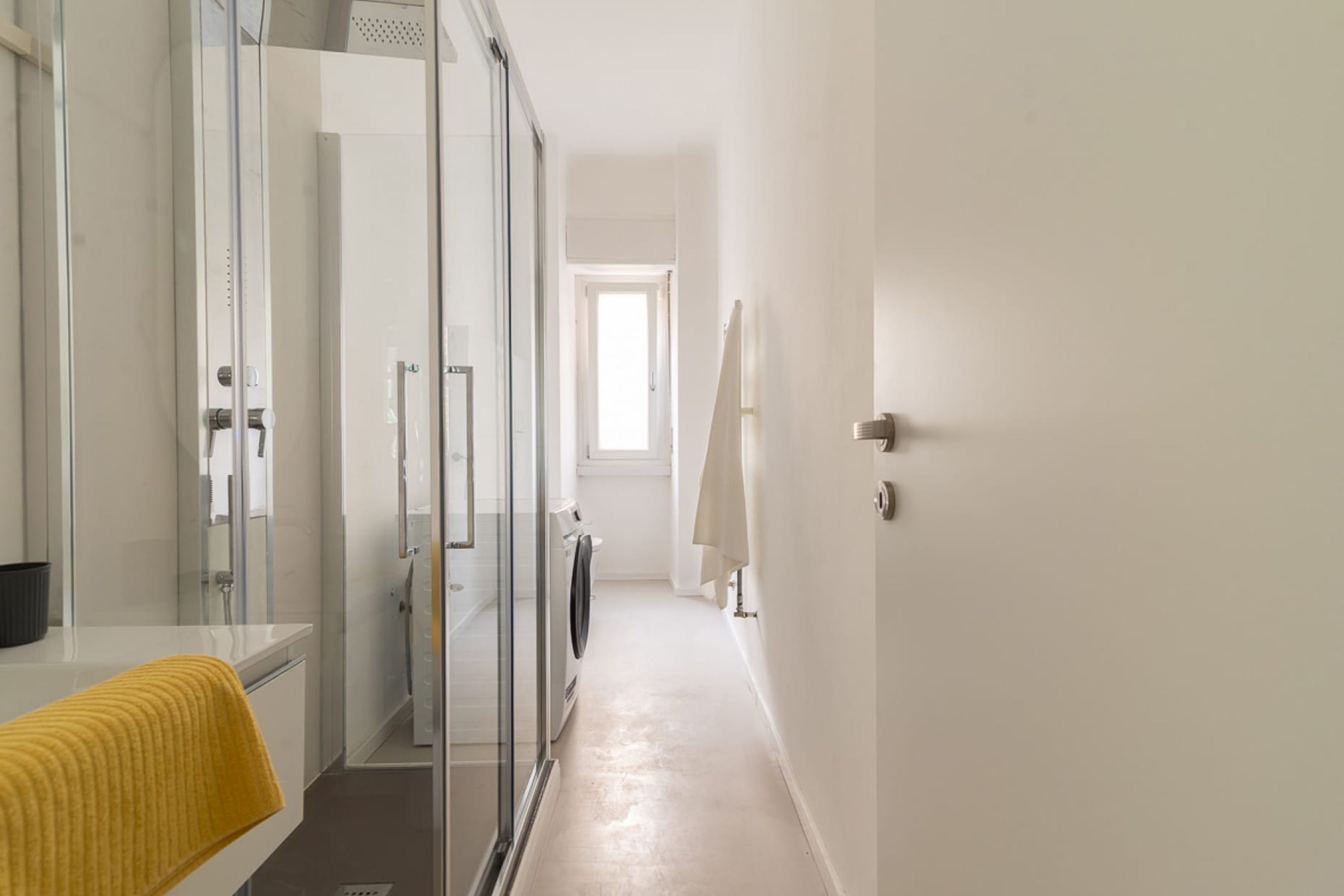 A modern bathroom with a glass shower enclosure, a white sink, and a yellow towel.