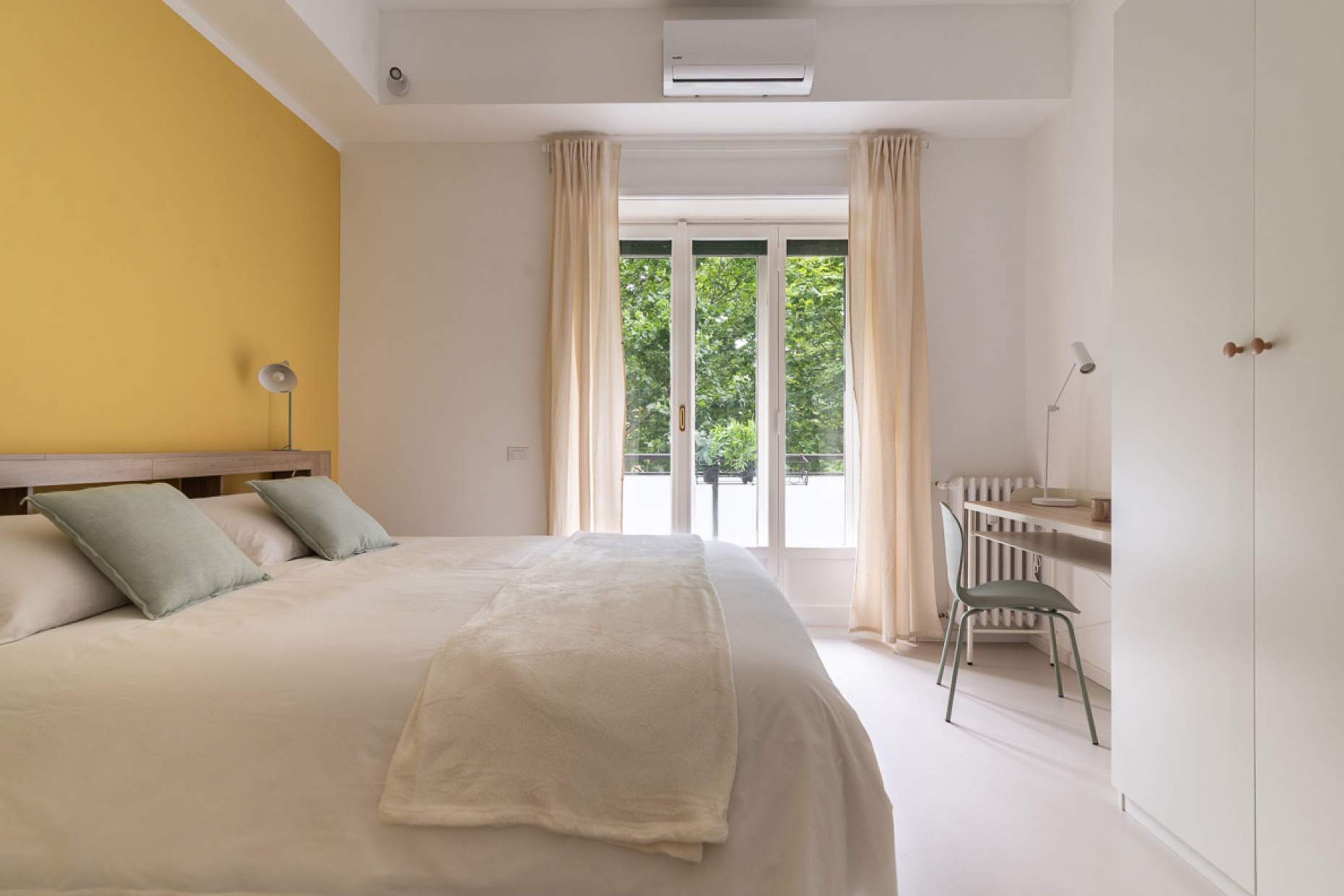 Ein Schlafzimmer mit einem großen Bett, einem Schreibtisch und Blick auf Grünflächen.