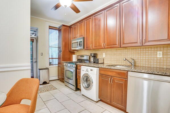 A kitchen with wooden cabinets, a microwave, an oven, a washing machine, and a sink. - Walk to Washington St: Hoboken Apt w/ Balcony! (Hoboken)
