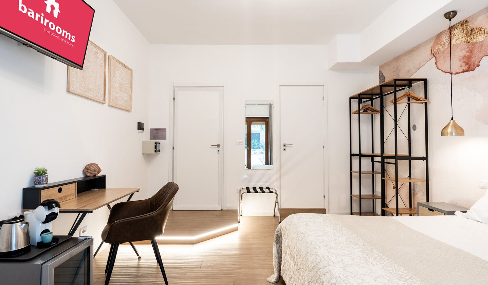 A hotel room with a bed, a desk, a chair, a wardrobe, and a TV displaying the barrooms logo.