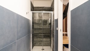 Un bany modern amb cabina de dutxa de vidre, parets de marbre i un moble de tocador de fusta.