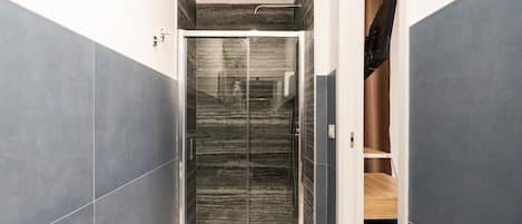 A modern bathroom with a glass shower enclosure, marble walls, and a wooden vanity.
