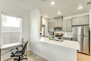A modern kitchen with stainless steel appliances, a white countertop, and a black office chair. - 2 Mi to Downtown Temple: Newly Built Townhome! (Temple)