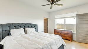 A bedroom with a tufted headboard, a large bed with white bedding, a wooden dresser, and a ceiling fan. - 2 Mi to Downtown Temple: Newly Built Townhome! (Temple)