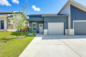 Ein modernes, zweistöckiges Haus mit Garage, einem Vorgarten mit kleinem Baum und wolkenlosem, blauem Himmel.
