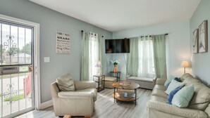 Una sala de estar con un sofá color beige, una mesa redonda de centro y un televisor montado en la pared.