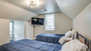 Un dormitorio con dos camas, un televisor montado en la pared y una ventana con persianas.