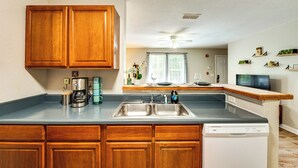 A kitchen with wooden cabinets, a dishwasher, a coffee maker, and a window with curtains. - Universities, Parks & More: Getaway in Tallahassee (Tallahassee)