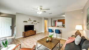 A modern living room with a flat-screen TV, a wooden coffee table, a sofa, and a dining area with two blue chairs. - Universities, Parks & More: Getaway in Tallahassee (Tallahassee)