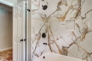 Un baño con pared de mármol, una bañera y una ducha.