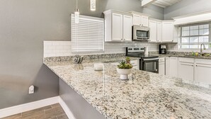 Cocina con armarios blancos, encimeras de granito, microondas, estufa y lámparas colgantes.