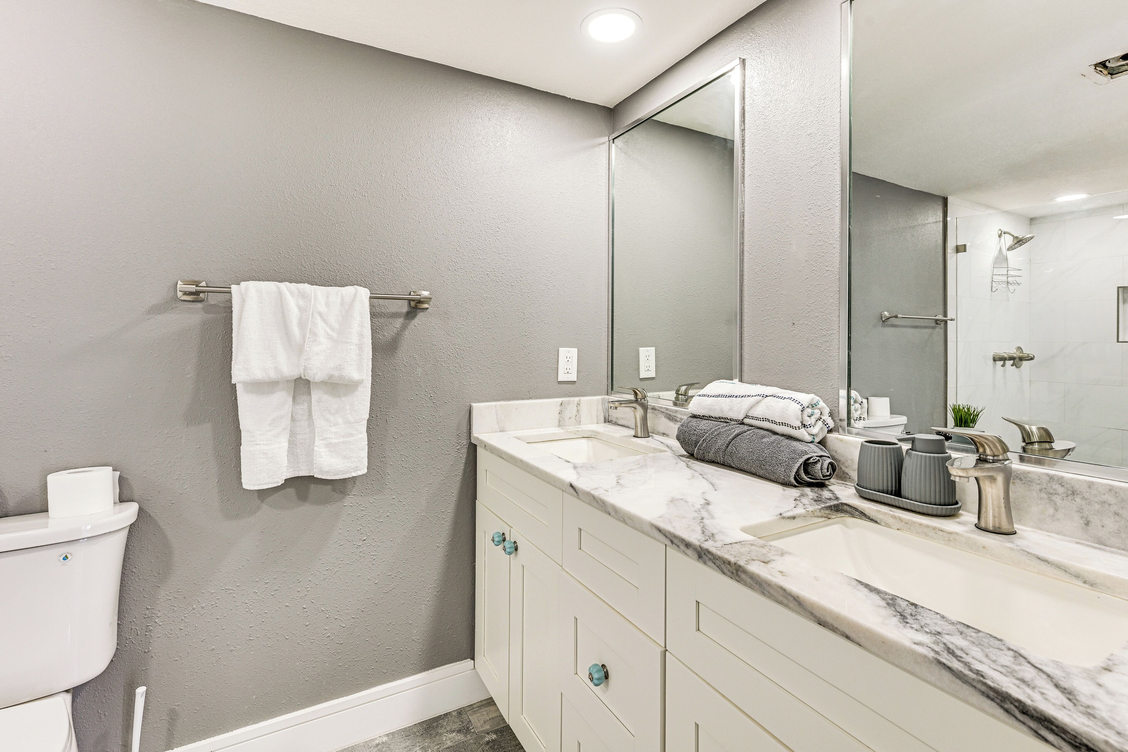 A modern bathroom with a marble sink, white cabinets, and a large mirror.