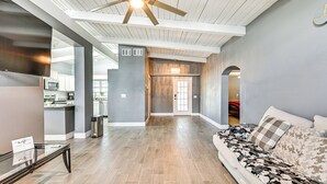 Un espacio habitable amplio con un ventilador de techo, un sofá con cojines estampados y una cocina al fondo.