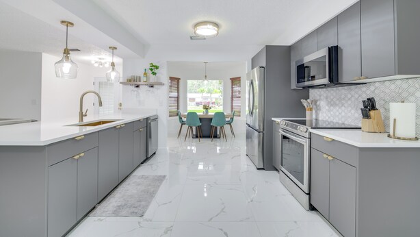 A modern kitchen with grey cabinets, a white countertop, and a central island. There is a dining area with two chairs and a table. - Swim, Hike & Kayak: Crystal River Retreat w/ Yard! (Crystal River)