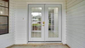 A white double door with a glass panel, set in a corner with white siding walls and a concrete floor. - Swim, Hike & Kayak: Crystal River Retreat w/ Yard! (Crystal River)