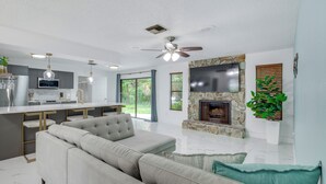 A modern living room with a sofa, a fireplace, and a TV mounted on the wall. - Swim, Hike & Kayak: Crystal River Retreat w/ Yard! (Crystal River)