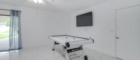 Een kamer met een pooltafel, een plafondventilator, een aan de muur bevestigde televisie en een deur.