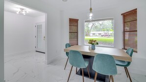 A dining area with a wooden table, four teal chairs, and a window with blinds. - Swim, Hike & Kayak: Crystal River Retreat w/ Yard! (Crystal River)