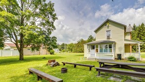 Una casa con porche, césped con mesas de picnic y un árbol.